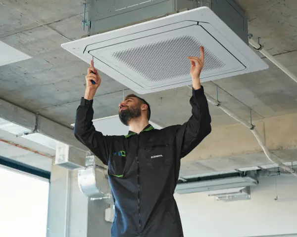 Técnico ajustando una unidad de cassette para la instalación de ventilación en un techo de hormigón.