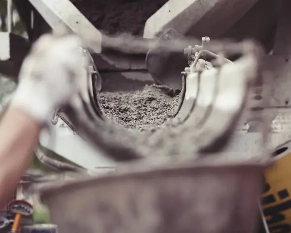 Ręka w rękawiczce kieruje strumień cementu do maszyny. Zastanawiasz się, ile kosztuje worek cementu?