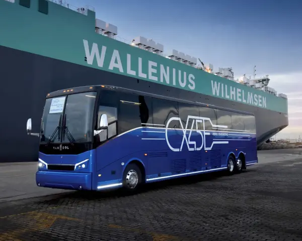 Niebieski autokar Van Hool CX45 z napisem "ZERO EMISSIONS" stoi przy ogromnym statku Wallenius Wilhelmsen.