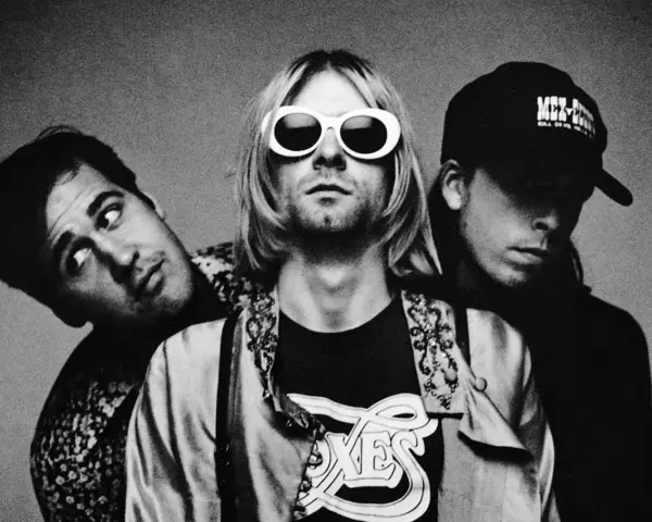 Les membres de Nirvana posent ensemble, Kurt Cobain au centre avec ses lunettes blanches iconiques.