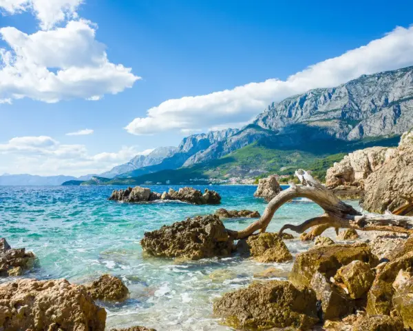 Piękne wybrzeże Chorwacji z turkusową wodą, skalistą plażą i górzystym krajobrazem w tle. Idealne miejsce, by zastanowić się, gdzie do Chorwacji.