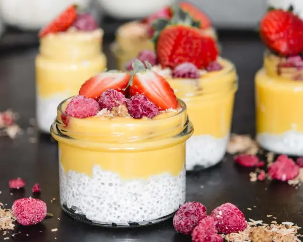 Erfrischender Mango Chia Pudding in Gläsern, garniert mit Erdbeeren und Himbeeren. Ein gesunder Genuss!