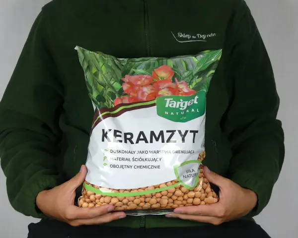 Osoba trzyma worek z napisem "Keramzyt", który jest doskonałym materiałem drenażowym i ściółkującym.