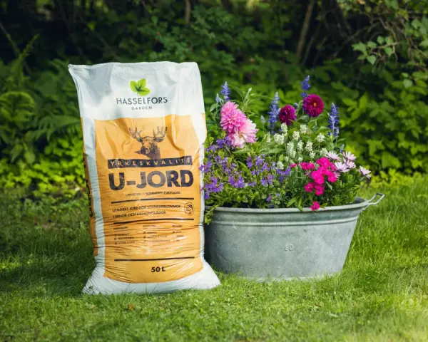 En säck U-jord från Hasselfors Garden står bredvid en zinkbalja fylld med färgglada blommor, redo att plantera.