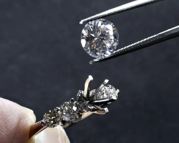 Un diamante viene posizionato con una pinzetta su un anello con incastonatura a castone ribattuto, pronto per essere fissato.