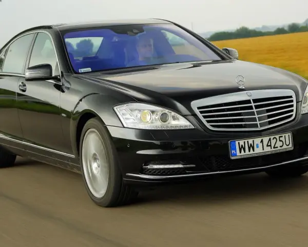 Czarny Mercedes-Benz W221 pędzi po drodze, mijając pola.