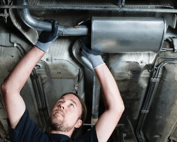 Mechanic working on a car's exhaust system. This tune up consists of replacing a section of the exhaust pipe and muffler.