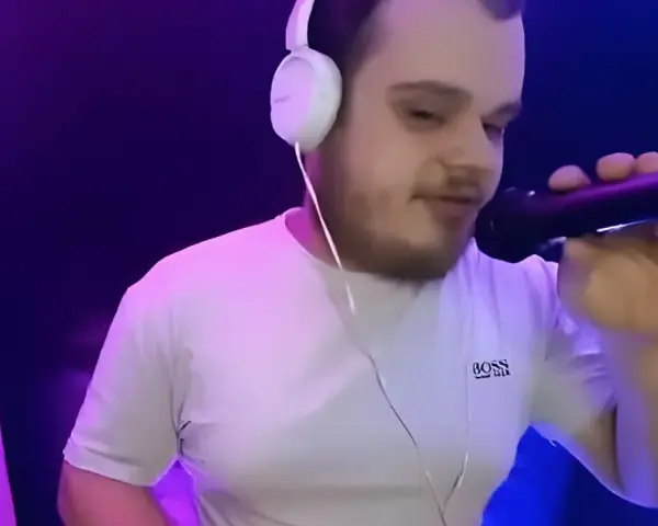 Młody dj akun w słuchawkach i białej koszulce z mikrofonem w ręku, w studiu z fioletowym oświetleniem.