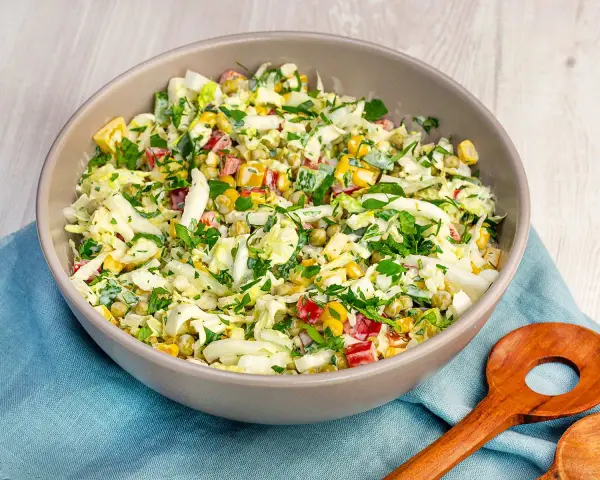 Schüssel mit knackigem Salat aus Weißkohl, Mais, Erbsen und Paprika, perfekt als salate zum vorbereiten am vortag. Mit frischer Petersilie garniert.