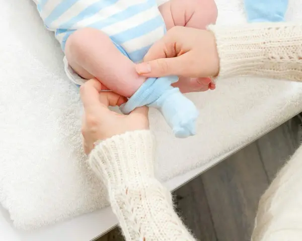Mama zakłada niebieskie skarpetki na nóżki noworodka. Dobieranie odpowiedni jaki rozmiar skarpetek dla noworodka jest ważne.