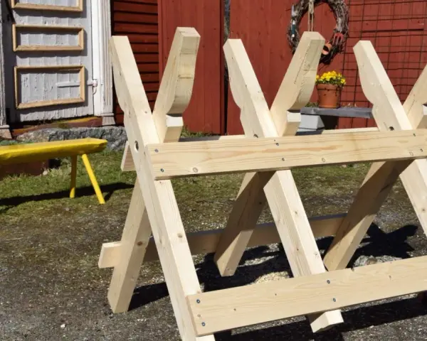 Nybyggd sågbock i trä, redo för att bygga ved. En gul bänk syns i bakgrunden.
