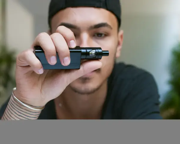 Joven con gorra negra sostiene un cigarrillo electrónico, mostrando sus claromizadores.
