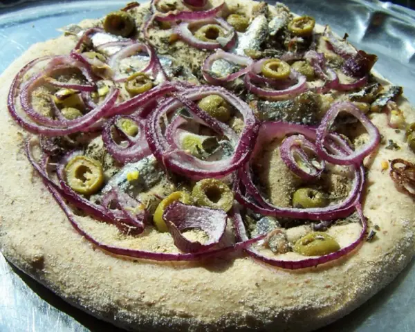 Pizza z anszua, oliwkami i czerwoną cebulą, gotowa do pieczenia.