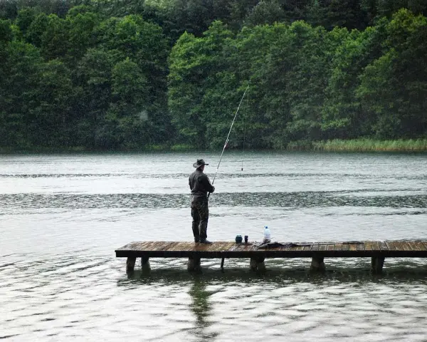 Ein Angler steht auf einem Steg und übt aus, wie angelt man, während es regnet.
