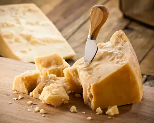 Kawałki Grana Padano i parmezanu na drewnianej desce. Nóż wbity w duży kawałek sera.