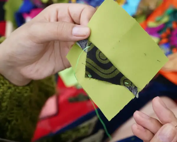 Ręce szyją zielone kwadraty z czarnym wzorem, tworząc patchwork projekty.