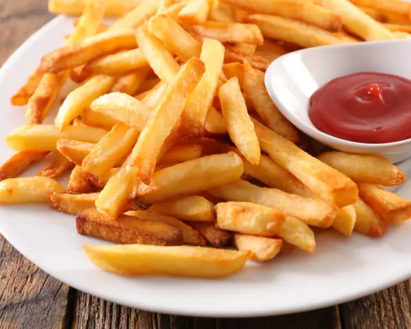 Une assiette de frites au four dorées et croustillantes, accompagnées d'un petit bol de ketchup rouge vif.