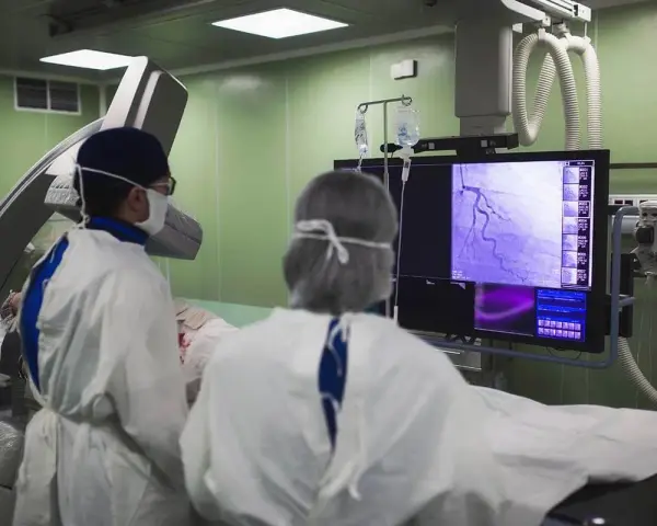 Lekarze w sterylnym stroju analizują obraz z koronarografii na monitorze w sali operacyjnej.