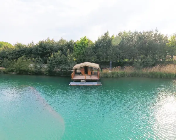 Drewniana chata na wodzie, otoczona lasem, unosi się na turkusowym zalewie.