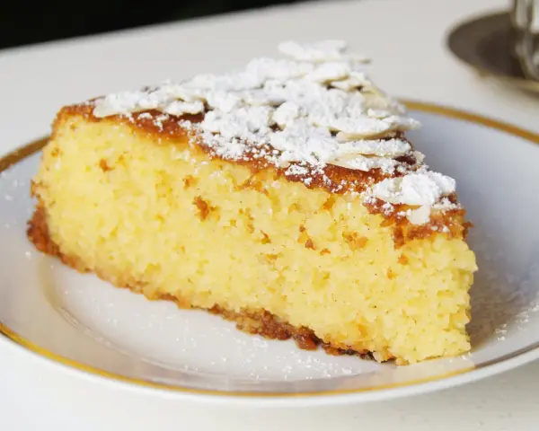 Rebanada de tarta de almendra esponjosa, espolvoreada con azúcar glas y láminas de almendra.