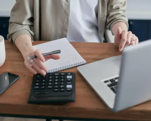 Persona revisa cuentas en su portátil, calculadora y libreta. Podría estar gestionando la hacienda pública deudora por IVA.