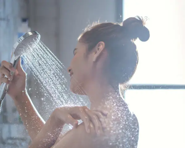 Donna sotto la doccia, l'acqua della doccia esce alternativamente calda e poi fredda, creando un effetto rinfrescante.