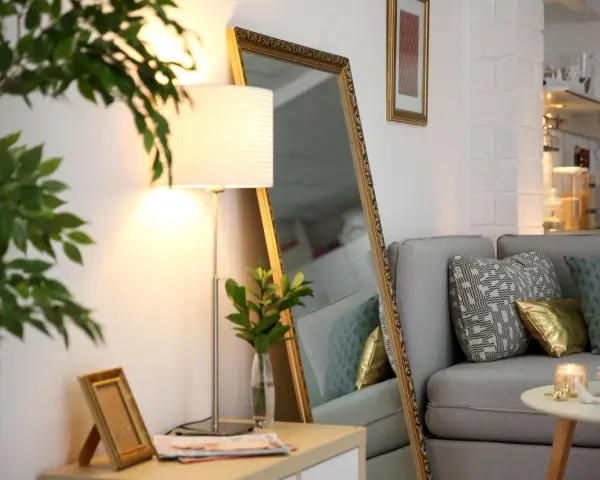 Ein großer Spiegel und eine Stehlampe helfen, die dunkle Wohnung heller zu machen. Ein Sofa mit Kissen und ein kleiner Tisch vervollständigen die Szene.