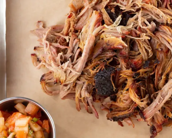Zartes Pulled Pork, perfekt gegart, zeigt die ideale pulled pork kerntemperatur. Daneben eine Schale mit frischer Salsa.