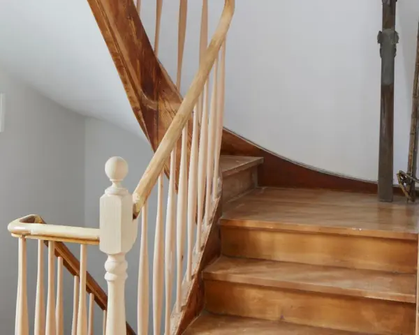 Eine alte Holztreppe wartet auf ihre Renovierung. Die Stufen und das Geländer aus hellem Holz zeigen Gebrauchsspuren, bereit für ein neues Leben.