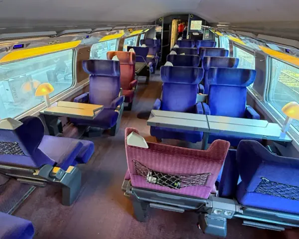 Interior of a bullet train, ready for a journey from Paris to Nice. Plush blue seats with tray tables line the carriage.