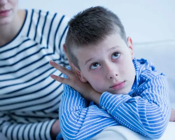 Bambino con sguardo pensieroso, forse durante un test autismo bambini 2 anni. La madre lo osserva con preoccupazione.