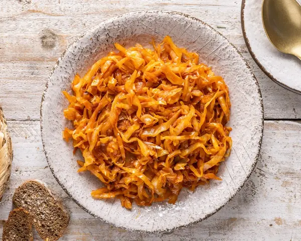 Un saporito cappuccio stufato in padella, servito in un piatto rustico, accompagnato da pane scuro e una posata dorata.