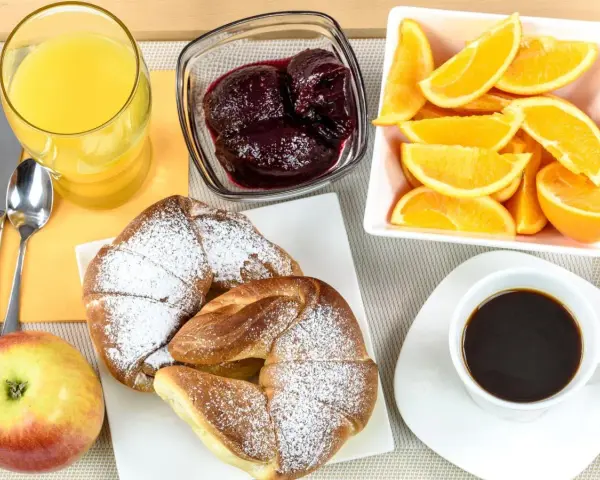Pyszne śniadanie kontynentalne: rogaliki z cukrem pudrem, pomarańcze, dżem, sok i kawa.