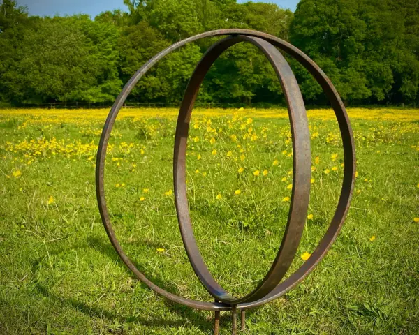 Metallskulptur im Feld mit gelben Blumen. Eine Idee, wie man ein Rondell im Garten gestalten kann, mit rustikalem Charme.