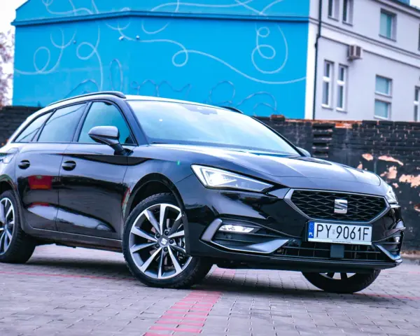 Czarny Seat Leon Sportstourer z polskimi tablicami rejestracyjnymi stoi na brukowanym placu przed budynkiem z niebieską, ozdobną ścianą.