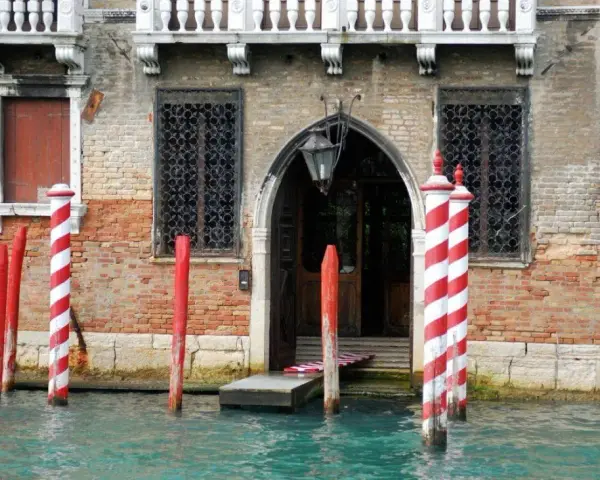 I pali di Venezia, chiamati bricole, segnano il canale davanti a un palazzo storico.