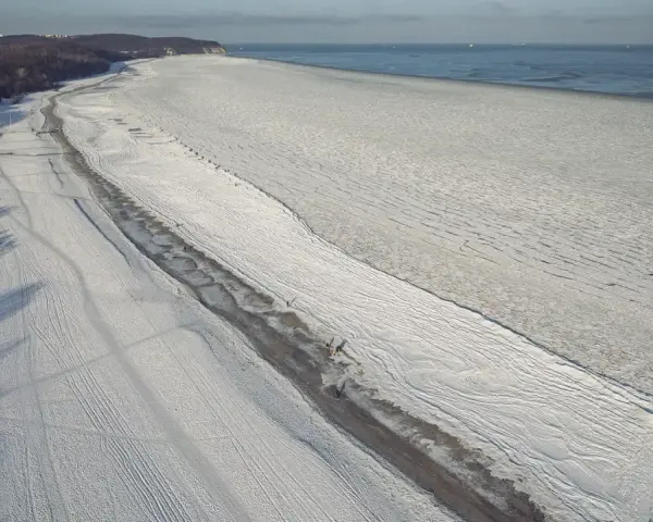Zamarznięta plaża i Bałtyk, jakby czas się zatrzymał od kiedy powstało morze bałtyckie. W oddali widać statki.