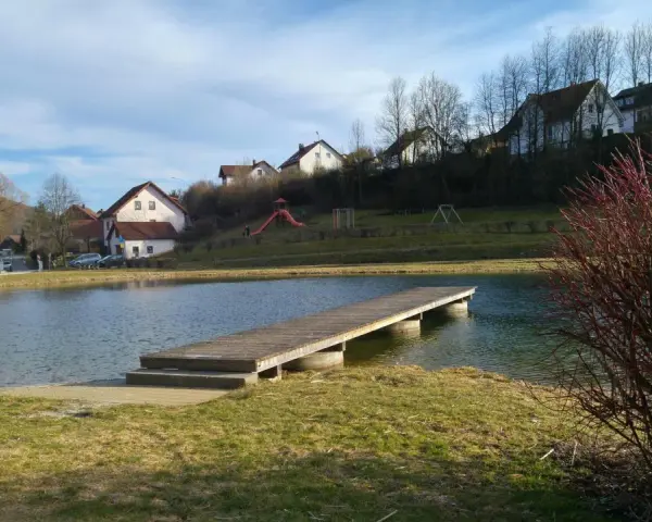 Holzsteg am Badesee Forchheim, mit Häusern im Hintergrund und einem Spielplatz.