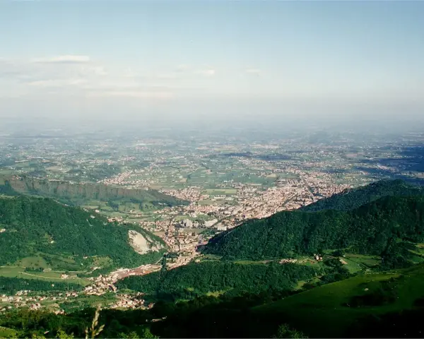 Vista panoramica dalla sella di Fadalto su una vasta pianura punteggiata di case e campi, con colline verdi in primo piano.