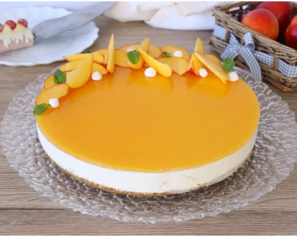 Delizioso cheesecake alle pesche con glassa lucida e fette di pesca fresca, guarnito con menta e piccole meringhe.