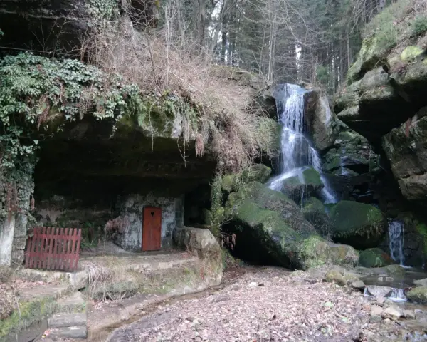 Ein versteckter Wasserfall bei Bad Schandau, mit einer kleinen Höhle und einer roten Tür.