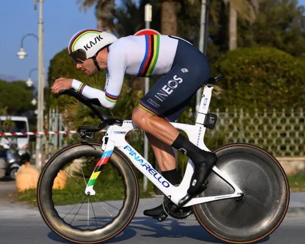 A cyclist in a rainbow jersey races a time trial bike, pushing hard during the Tour de France.