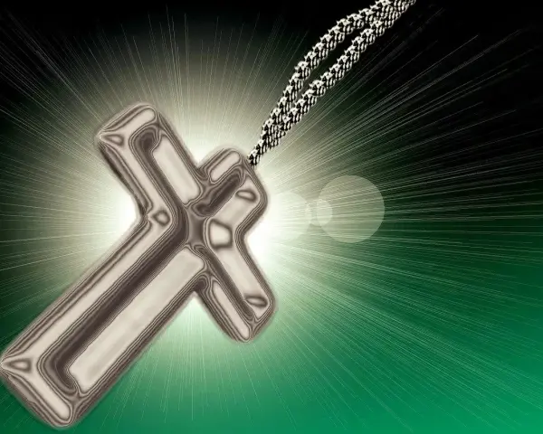 Metalowy krzyż na sznurku, otoczony blaskiem. Symbolizuje nadzieję i nawrócenie, światło rozchodzące się na zielonym tle.