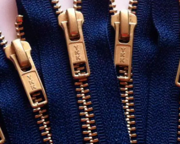 Primer plano de varias partes de una cremallera YKK dorada sobre tela azul.