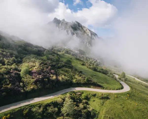 Strada tortuosa che sale verso le vette nebbiose, evocando l'ascesa al **Col du Tourmalet**.
