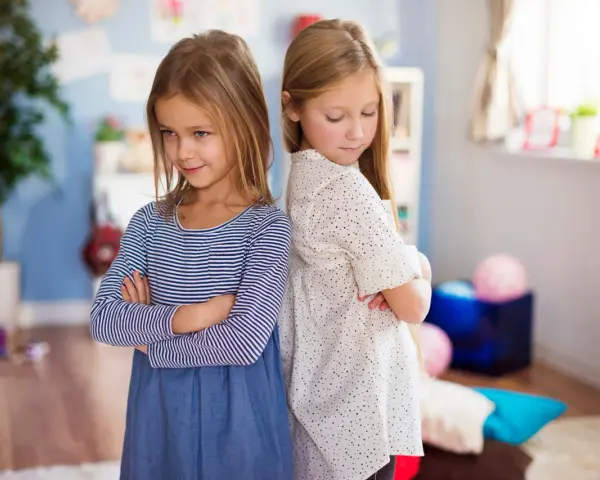 Dwie dziewczynki stoją plecami do siebie ze skrzyżowanymi rękami. W tle pokój dziecięcy. Jak nie zwariować ze swoim dzieckiem?