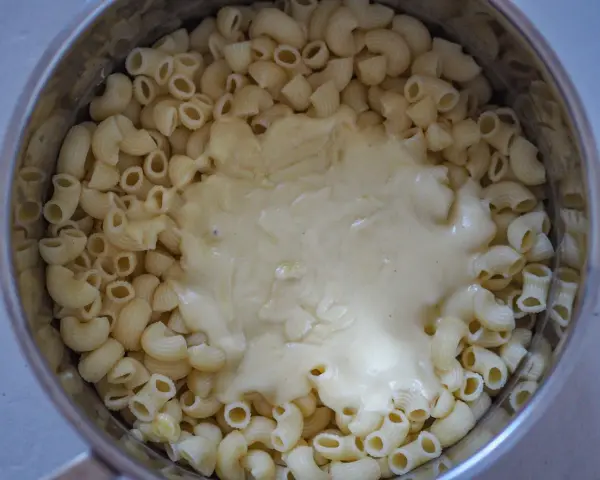 Gęsty, kremowy sos serowy otula makaron w garnku, tworząc pyszny makaron mac and cheese.