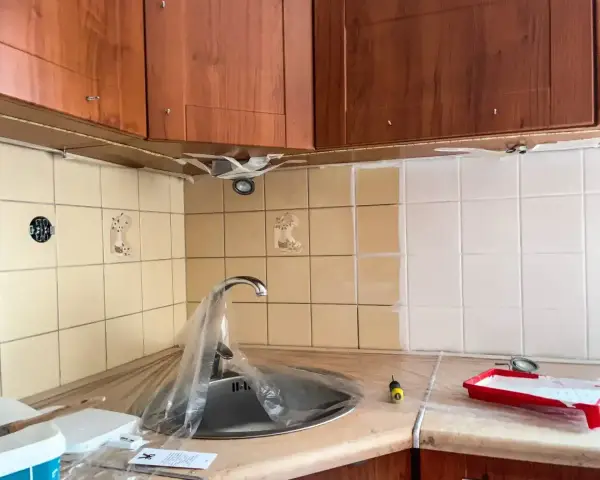 Malowanie starych płytek w kuchni na biało. Widać przygotowania do metamorfozy: farba, wałek i zabezpieczony zlew.