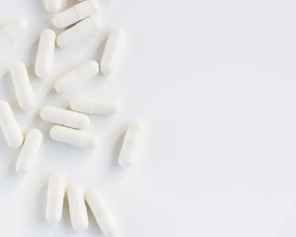 Vita kapslar utspridda på en vit yta. Kan dessa orsaka l-glutamin biverkningar?