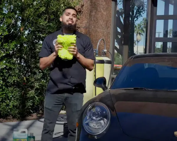 Man holding a fluffy wash mitt, ready to demonstrate how to wash a convertible car.